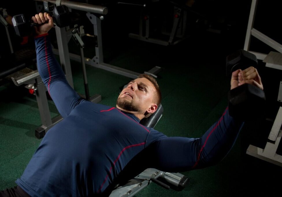 Young man pumping his arm muscles with barbells in gym